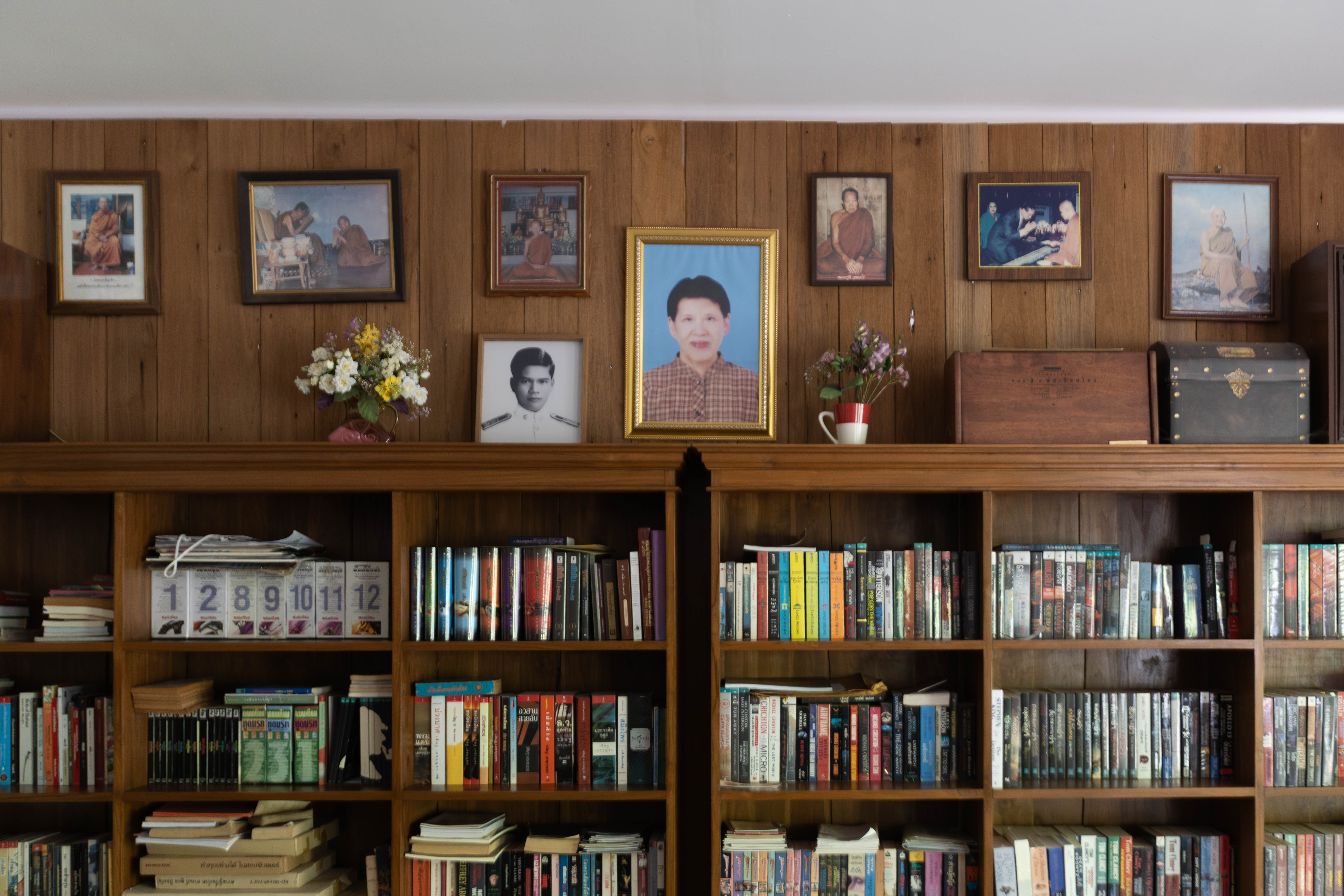A bookcase full of books in Thail and English with framed photos standing on top
